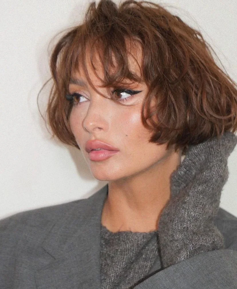A copper brown bob sits above the jaw with side swept waves and airy layers around the ears