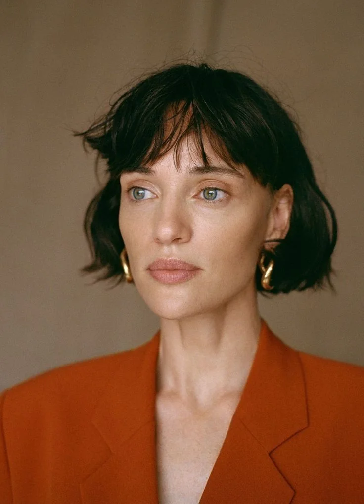 A deep black bob ends near the jaw with a short uneven fringe and a softly tucked perimeter