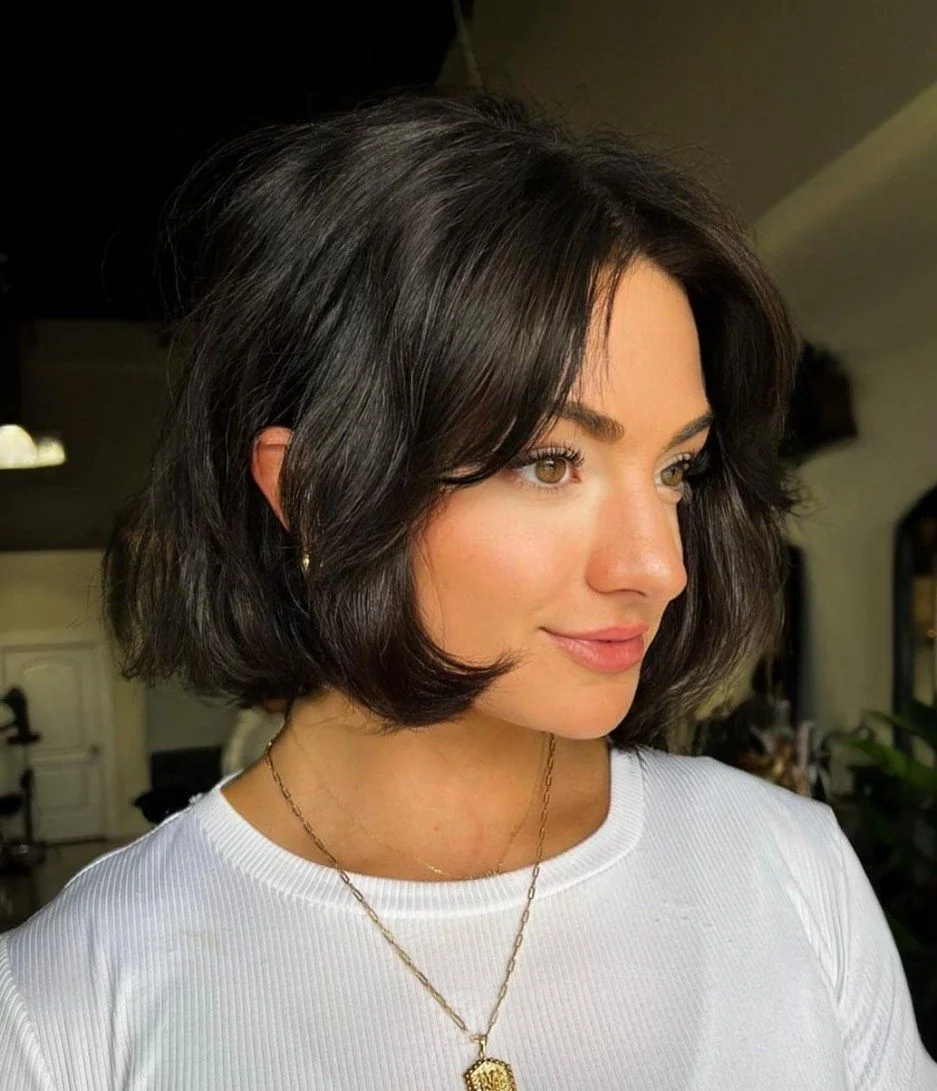 A dark brunette bob curves under the jaw with long front layers and a smooth center part