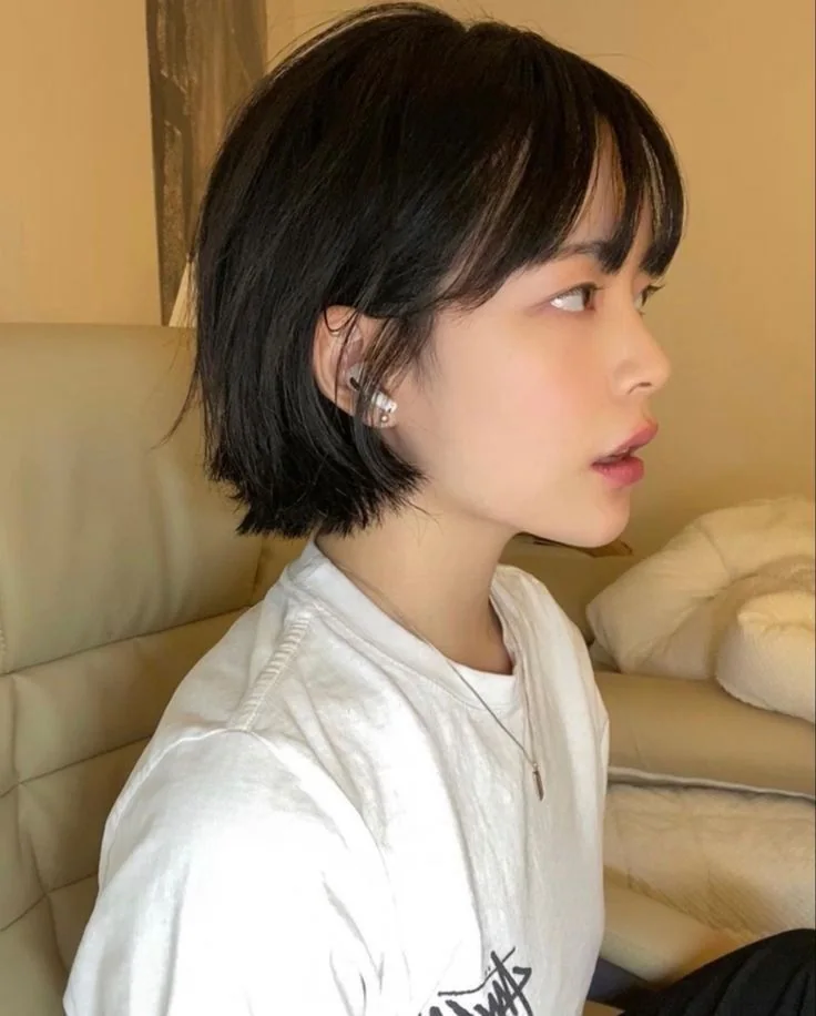 A sleek black bob sits close to the jaw with fine wispy bangs and subtly separated ends