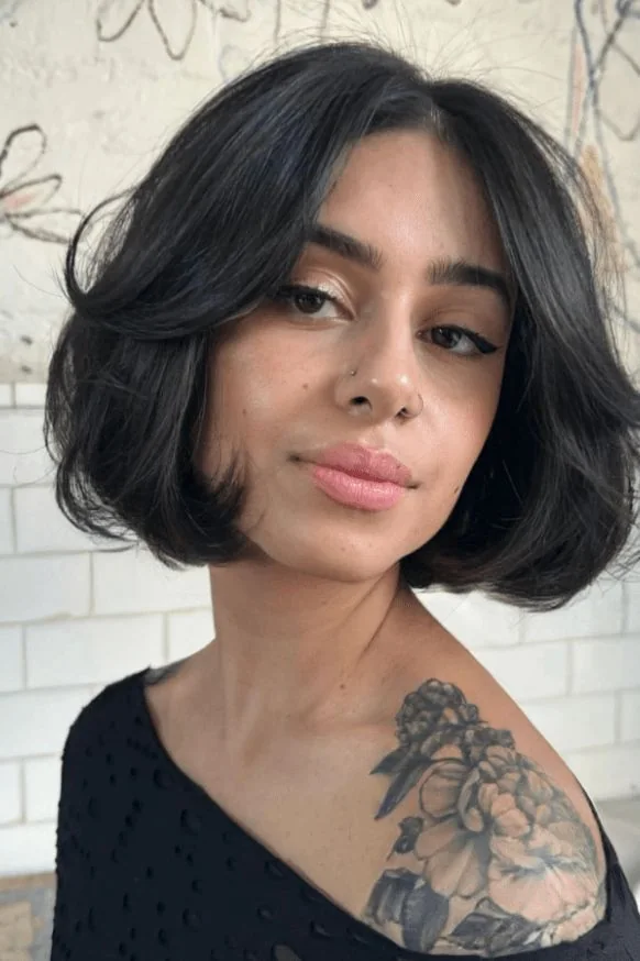 A full black bob curves beneath the jaw with center parted curtain pieces and softly lifted sides