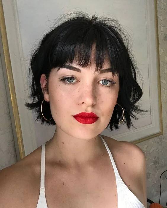 A short black bob has a cropped fringe, feathered sides, and fine ends kicked away from the jaw
