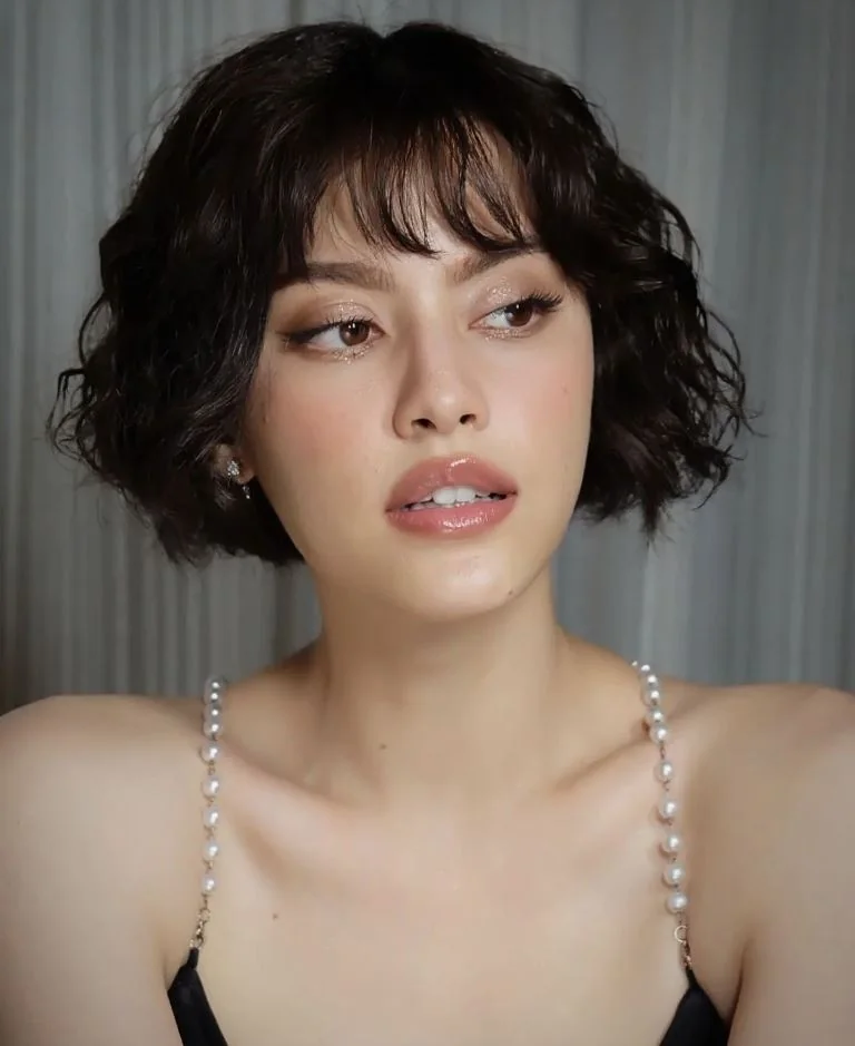 A short black bob uses loose curls, soft broken bangs, and rounded volume around the ears