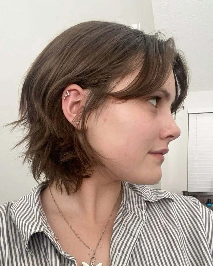 A brown shaggy bob falls near the neck with long curtain bangs and flicked layers at the sides and back
