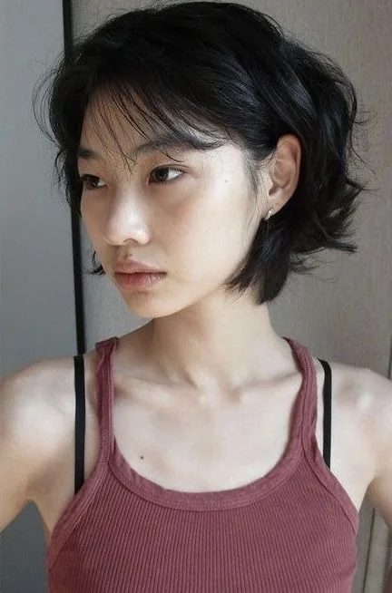 A dark bob has airy waves, an off center part, and a light tapered edge near the jaw