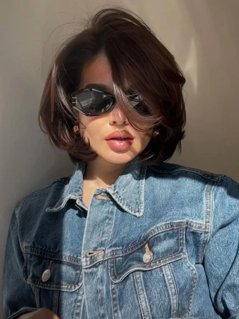 A dark brunette bob has broad face framing layers, strong side volume, and ends curled beneath the jaw