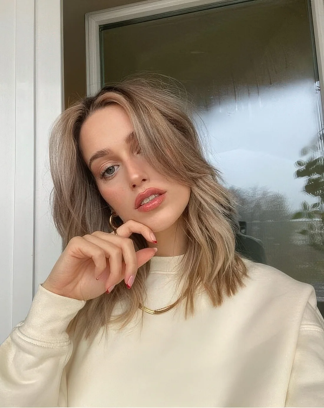 Mushroom blonde shade, medium wavy hair and long curtain bangs for a stylish and relaxed look.