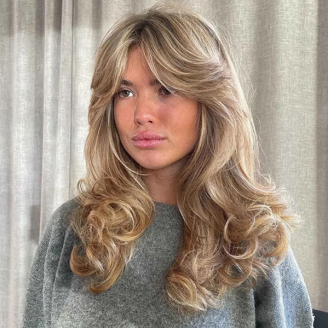 Long blonde hair with layers to remove weight, curls at the ends and soft curtain bangs.