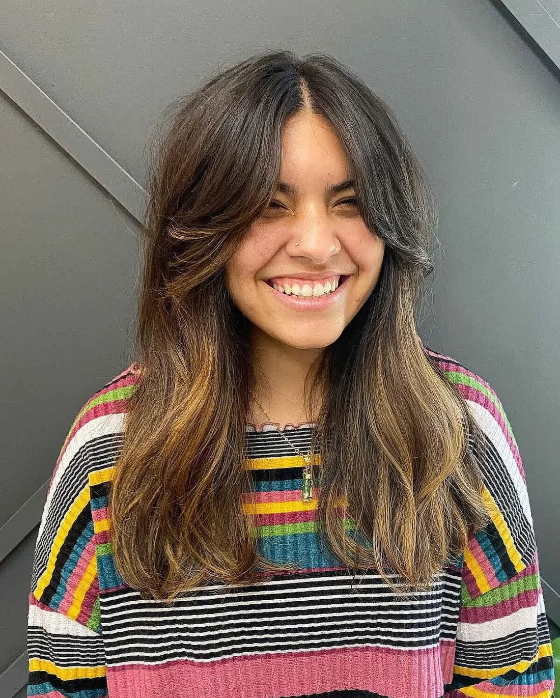 Long dark brown hair with a melted balayage and soft layered curtain bangs.