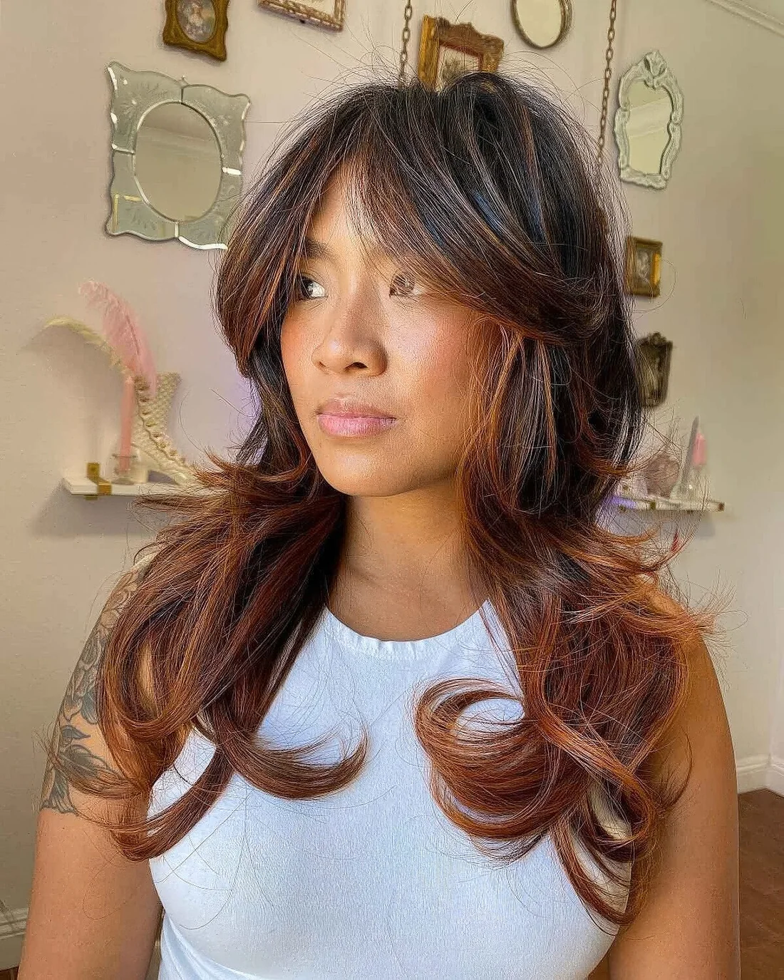 Long dark hair with caramel balayage, curls and soft curtain bangs.