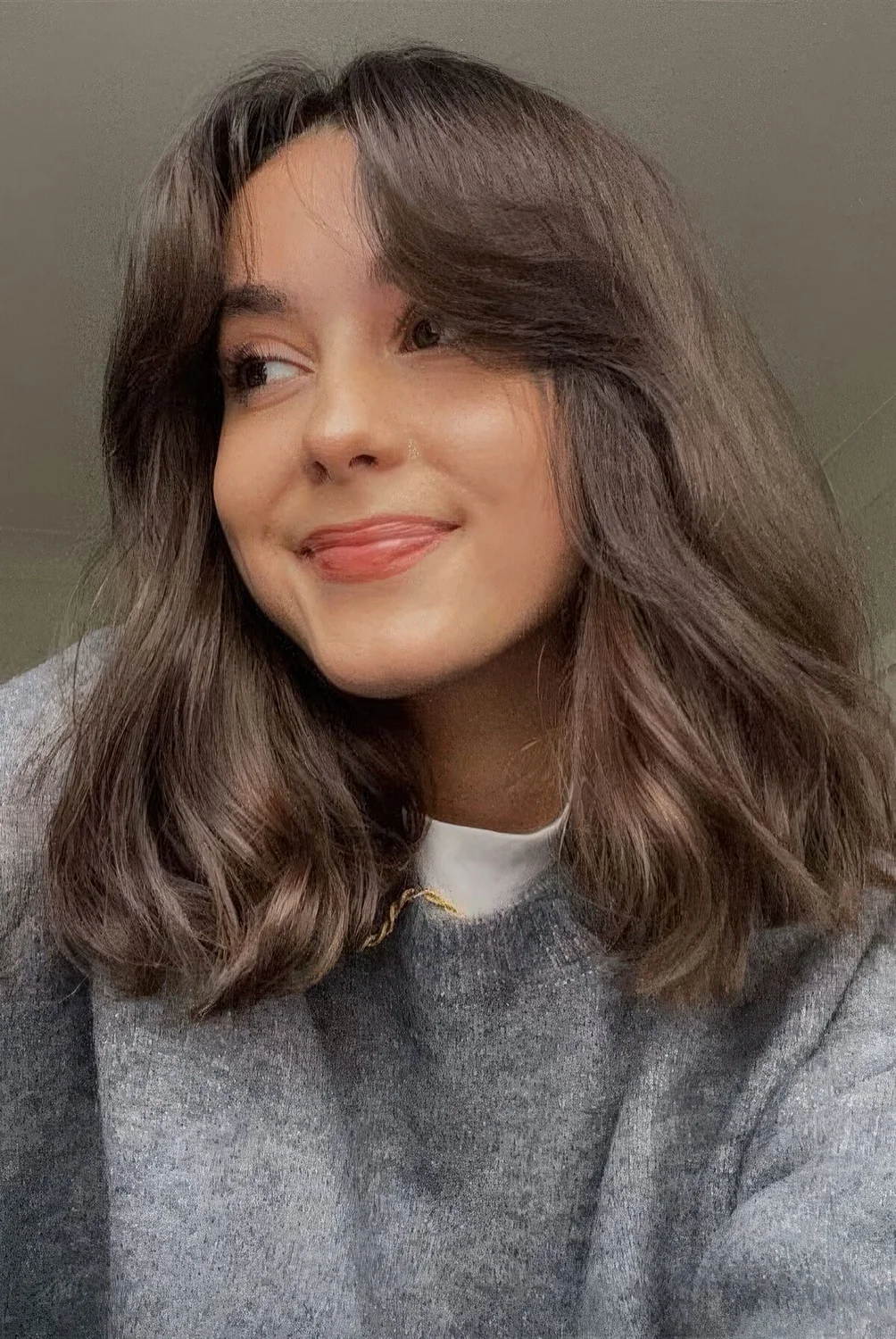 Medium-length brown hair with soft curtain bangs and slight waves on the ends.