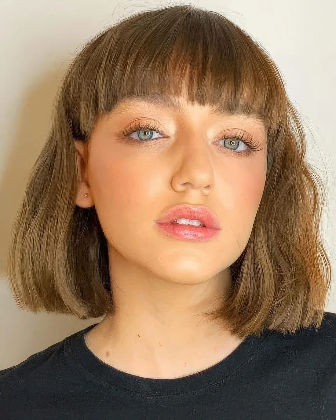 Light brown to caramel blunt bob on thick hair, with bangs and waves.