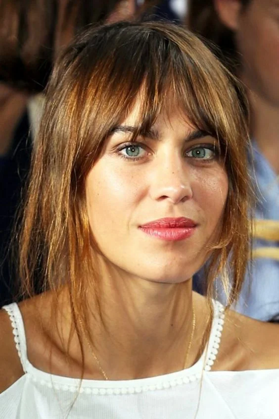 Alexa Chung rocking light brunette hair with slight caramel highlights and long layered bangs for a catchy look when wearing an updo.