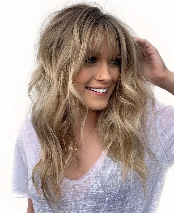 Long wavy londe hair with texture and with balayage plus layered bangs for a chic touch.