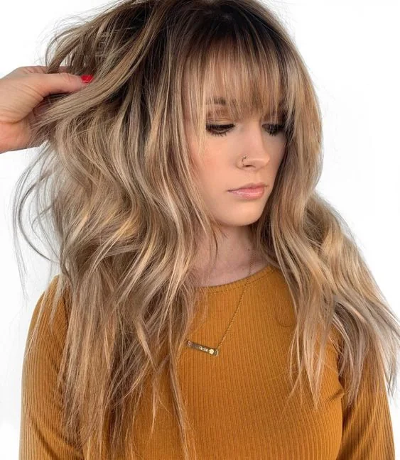 Long honey blonde hair with layered bangs and waves.