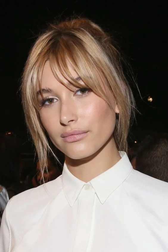 Hailey Baldwin wearing a blonde updo with layered bangs to frame the face in a delicate way and add interest to the look.