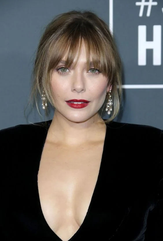 Light hair with caramel highlights in an updo and with layered bangs to frame the face in a beautiful way.