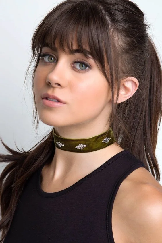 Long dark brown hair in a high ponytail and with layered bangs for a cuter and more girlish look.