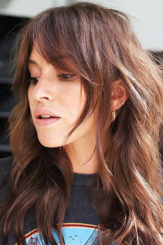 Long auburn wavy hair with layered curtain bangs.