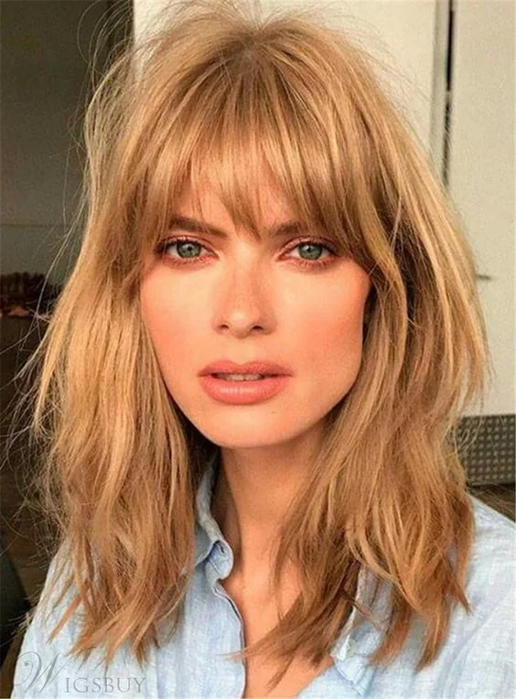 Medium-length messy and shaggy warm caramel blonde hair with layered bangs that that catch the eyes.