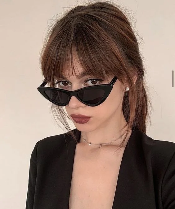 Brown hair in a low ponytail and with auburn highlights plus layered bangs for a bolder look.