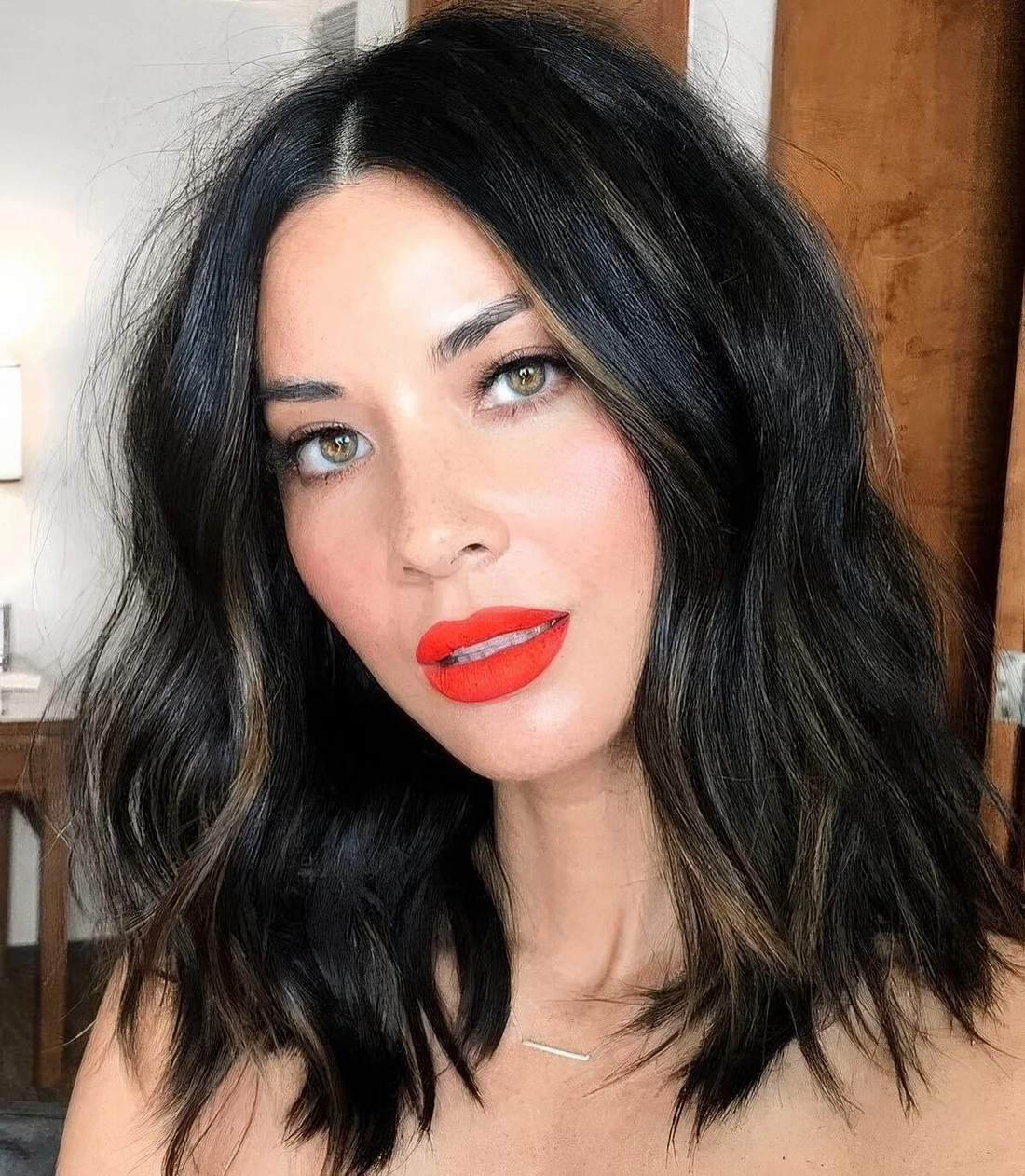 Black wavy and textural outgrown bob with honey highlights, middle part and much volume.