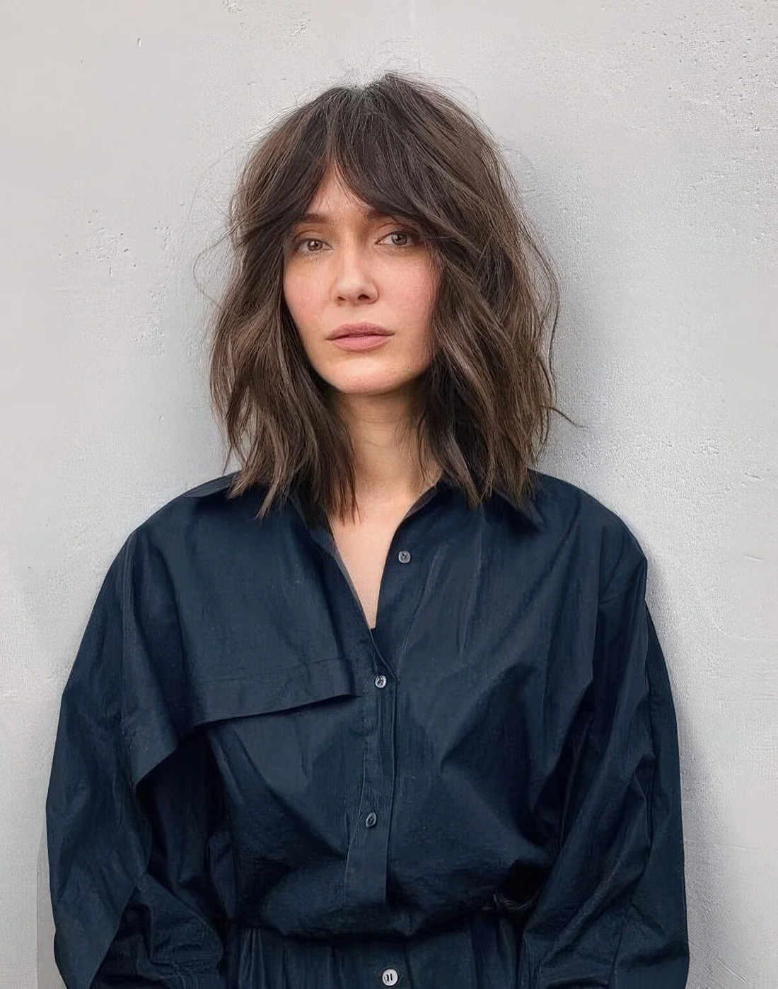 Brown outgrown bob with slight highlights, messy waves and bottleneck bangs.