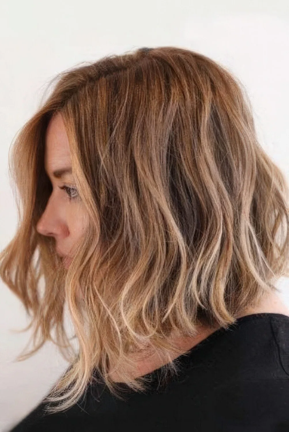 Light brown angled bob with honey balayage, side part, waves and texture.