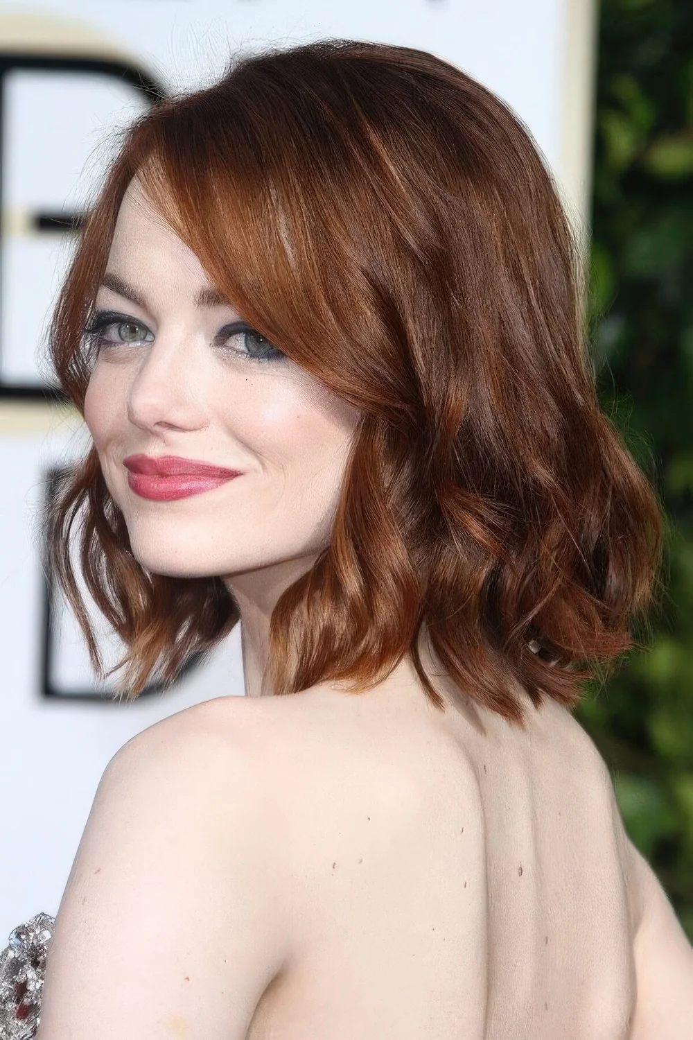 Emma Stone wearing a ginger red long bob with side part and waves.