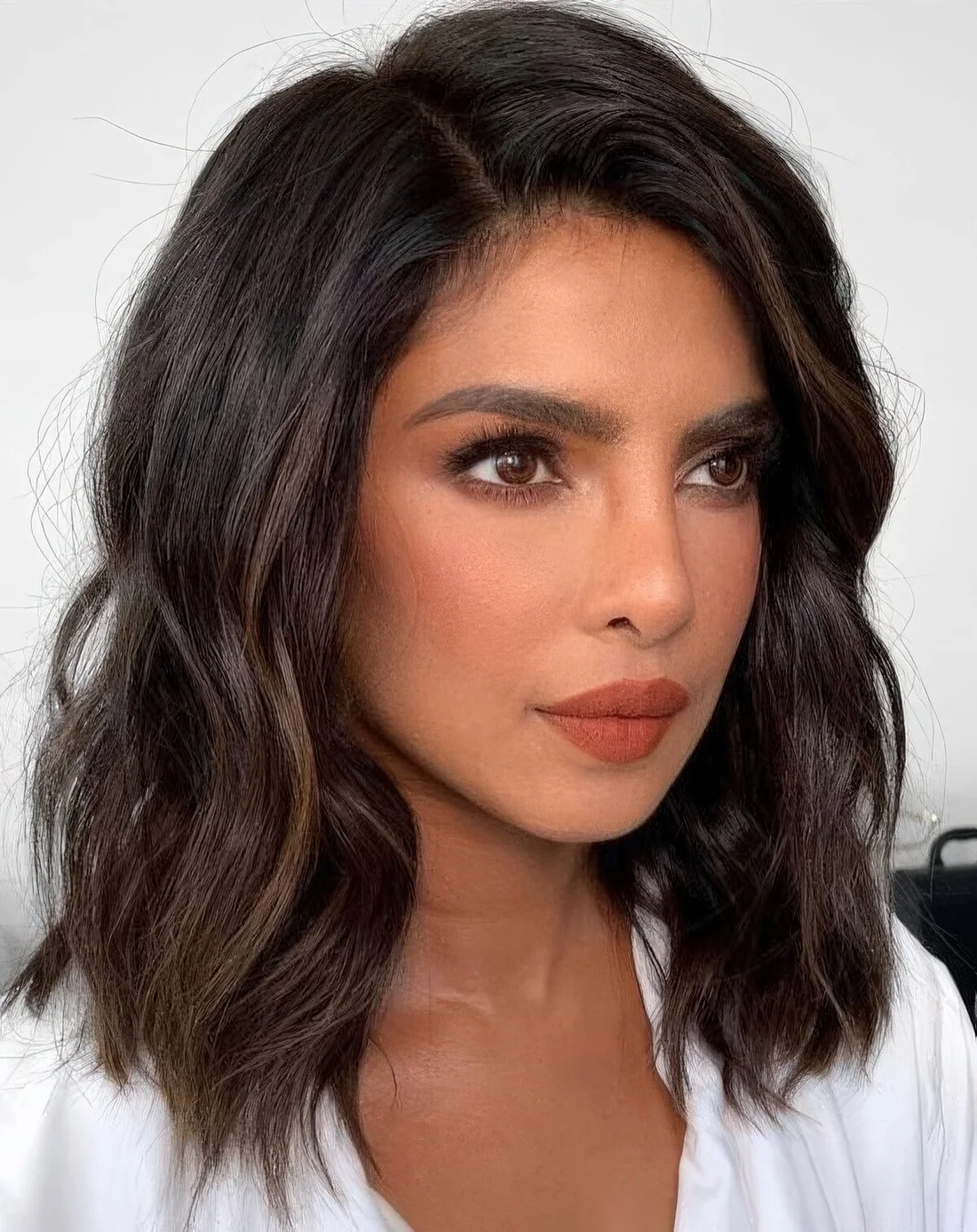 Priyanka Chopra wearing a black wavy outgrown bob with caramel highlights and side part plus a lot of volume.