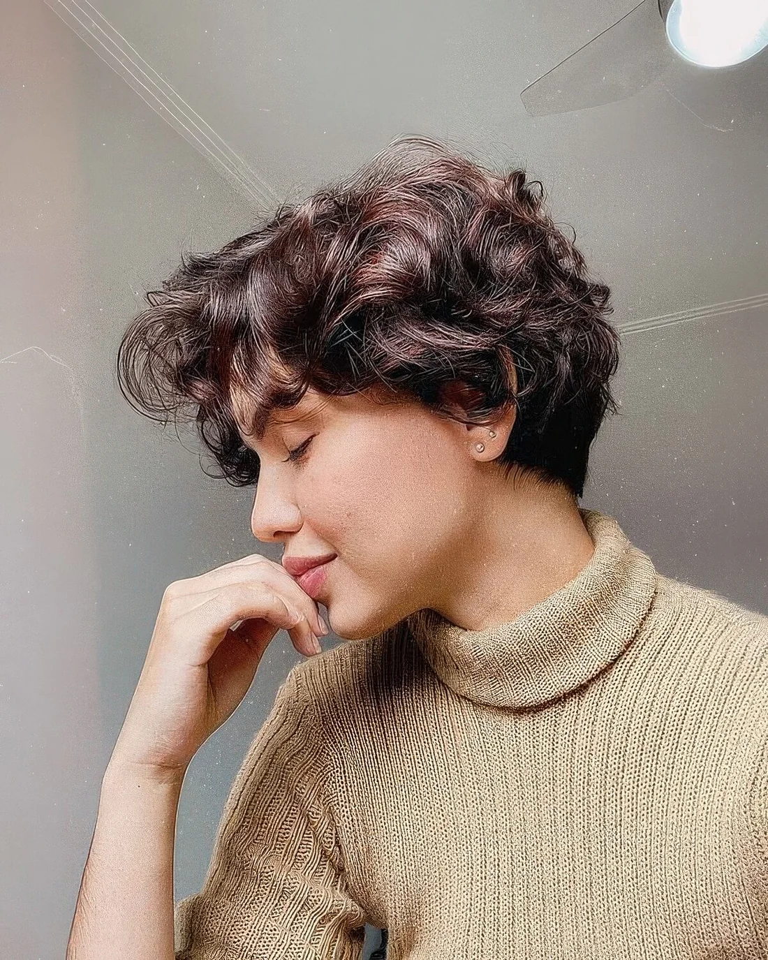 Dark brown wavy and curly pixie with a bit of short bangs.