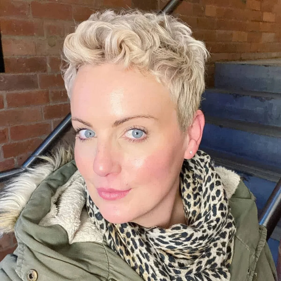 Short blonde wavy pixie haircut with some extra length on the sides and back and it.