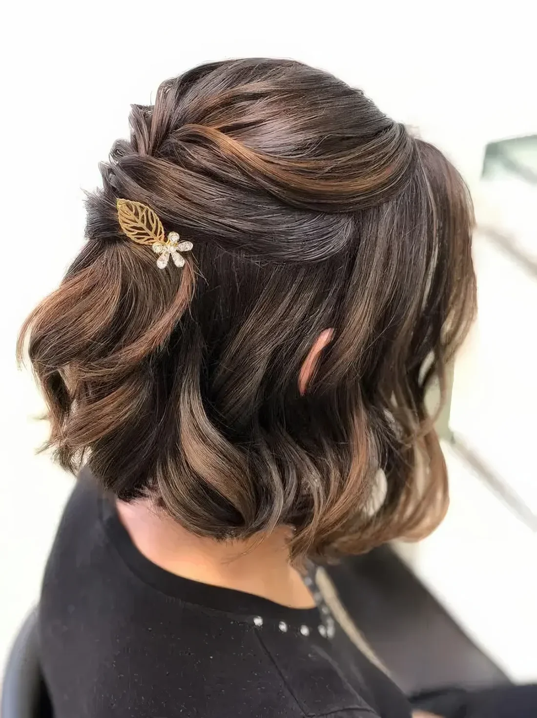 Refined half updo on medium-length hair with twists and waves down, a little leaf and flower hair pin and face-framing locks.