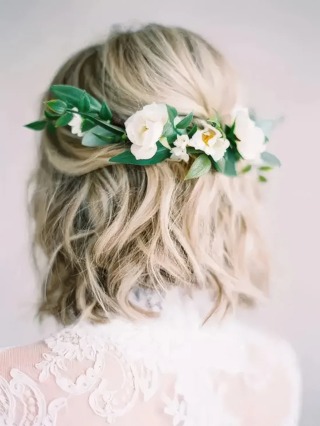 Wavy hairstyle with fresh white blooms and greenery on the back for a romantic bride.