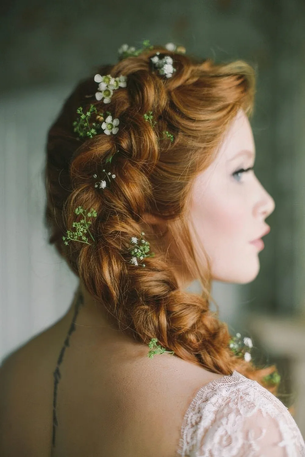 Side braid coming from the top of the head and accented with greenery and white blooms.