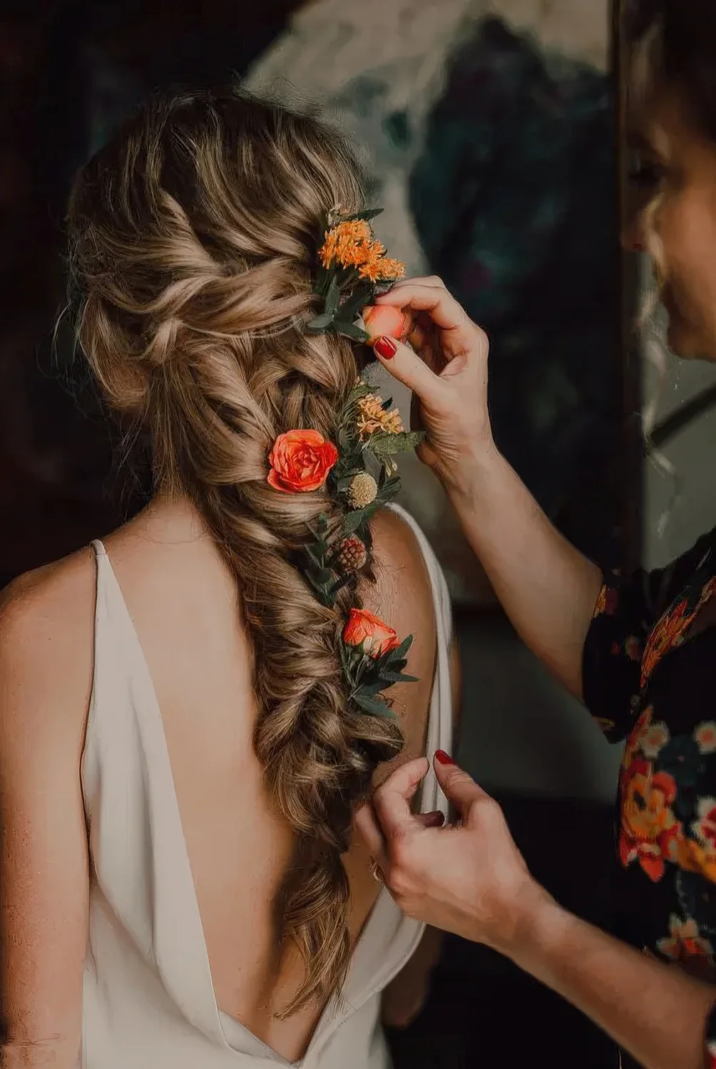 Loose and messy long braid with bold flowers and greenery tucked in.