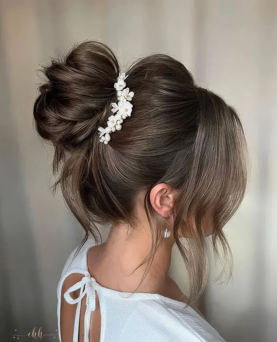 Messy top knot with a volume on top and face-framing hair plus a floral hair piece.