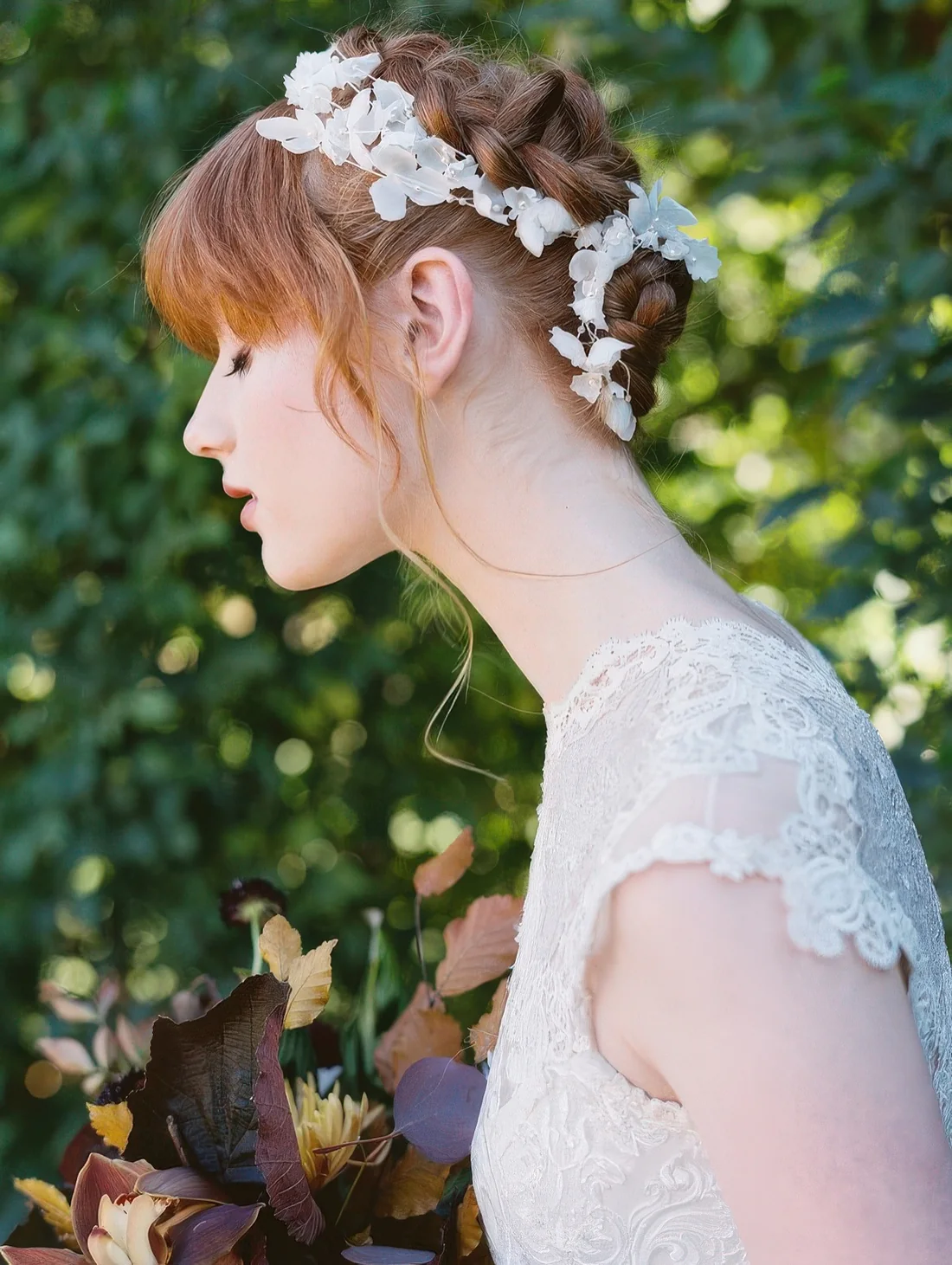 Fully braided updo with a white floral hair vine and bangs for a subtle and chic bridal look.