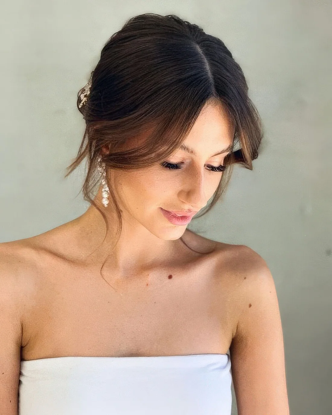Simple low updo with long curtain bangs and center part are a lovely and effortless idea for a wedding.