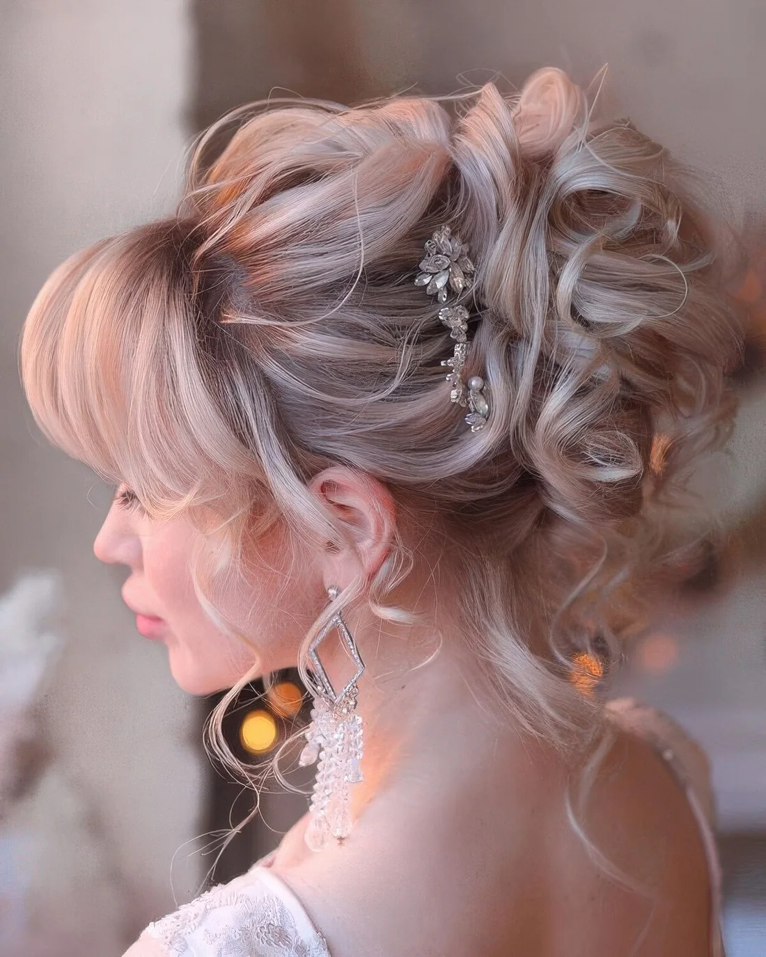 Sophisticated curly updo with a bump on top and layered bangs plus a rhinestone hairpiece.