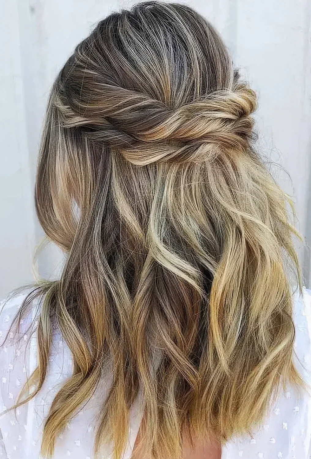Relaxed half updo with a bump on top, a double twisted halo and waves down.