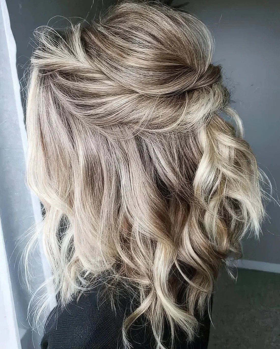 Blonde half updo with a bump on top and a twisted element and waves down.