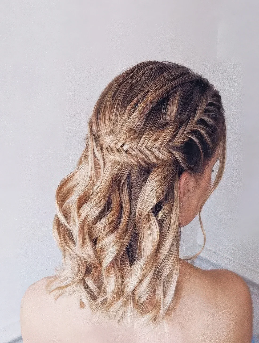 Boho wedding half updo on medium hair, with a large fishtail braid on one side and waves down.