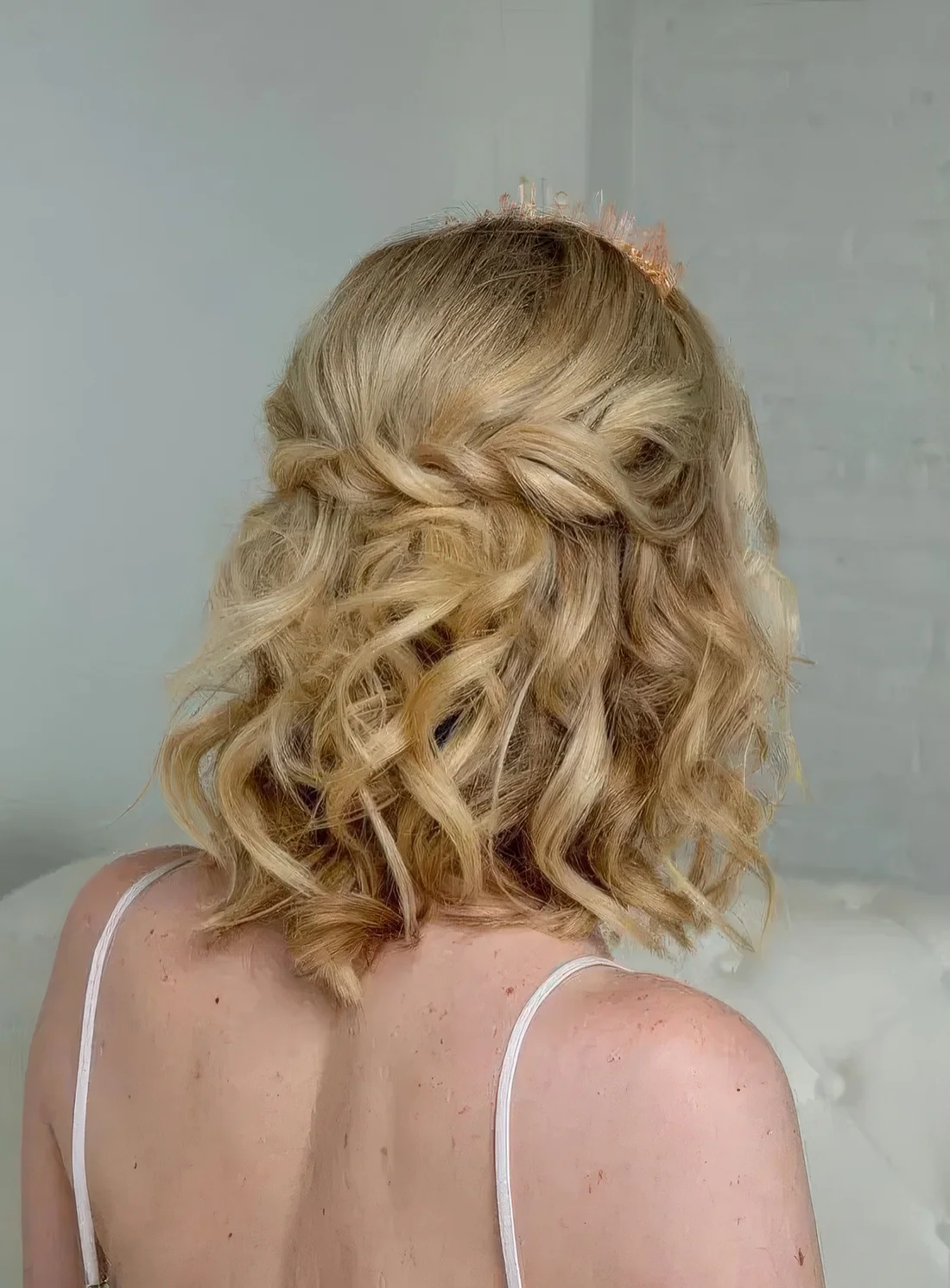 Curly half updo with a twisted braid and curls down plus a peachy crystal crown are a cool combo.