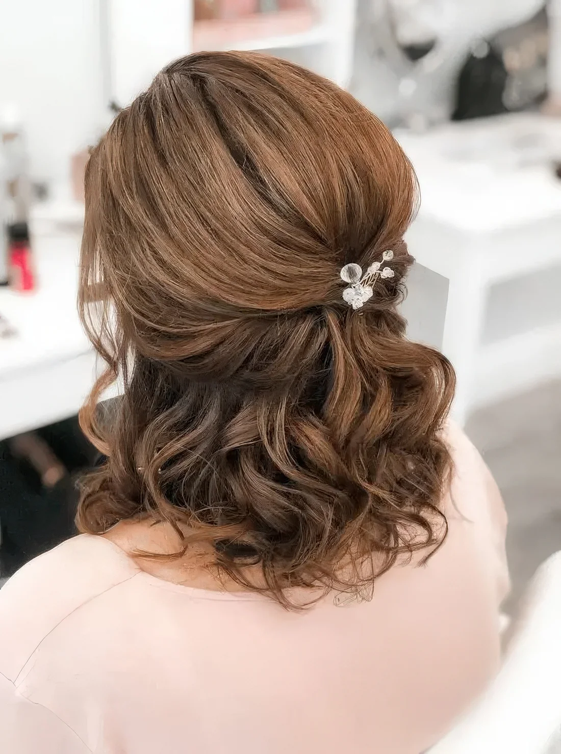 Half updo with a bump on top, waves down and face-framing hair with a rhinestone hair pin.