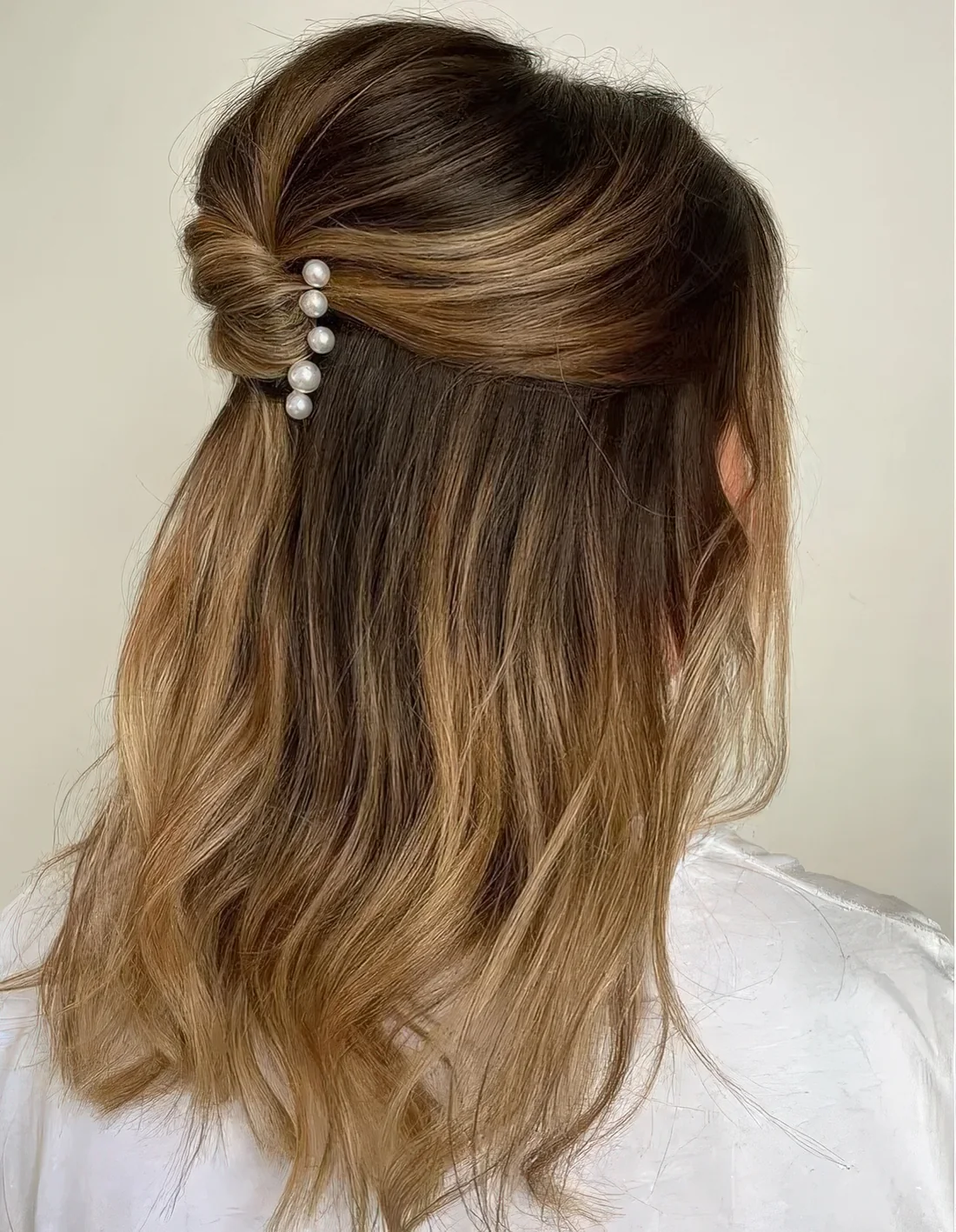 Half updo with a bump on top and a twist accented with pearl hair pins.