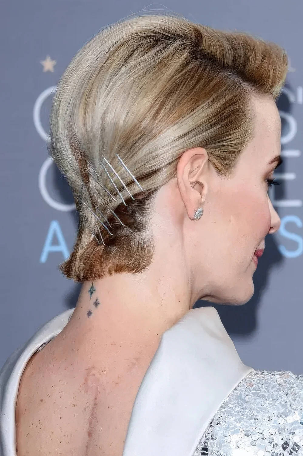 Blonde bixie with a darker root and some hair pins on the back.