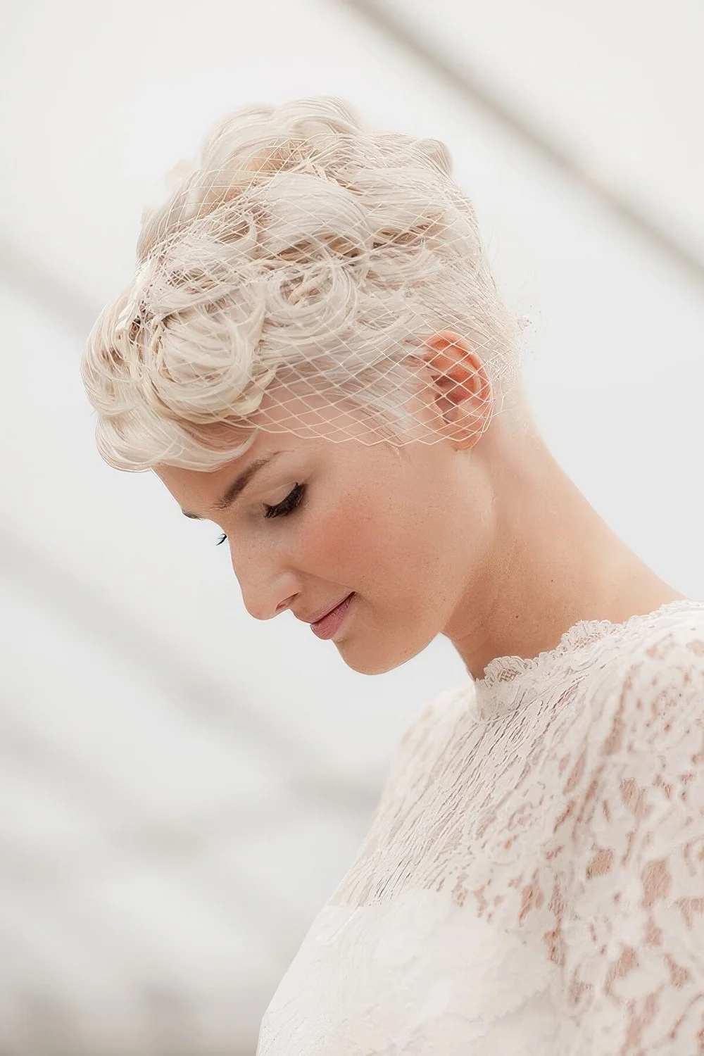 Curly platinum blonde pixie haircut with a small brdcage veil.