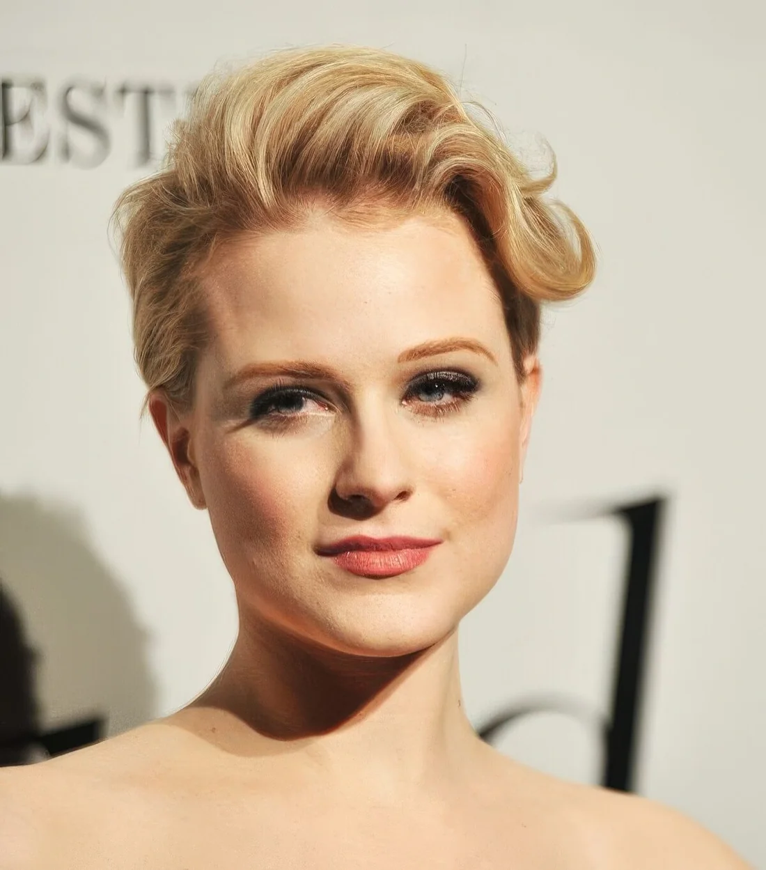Long warm blonde pixie haircut with waves styled to one side only.