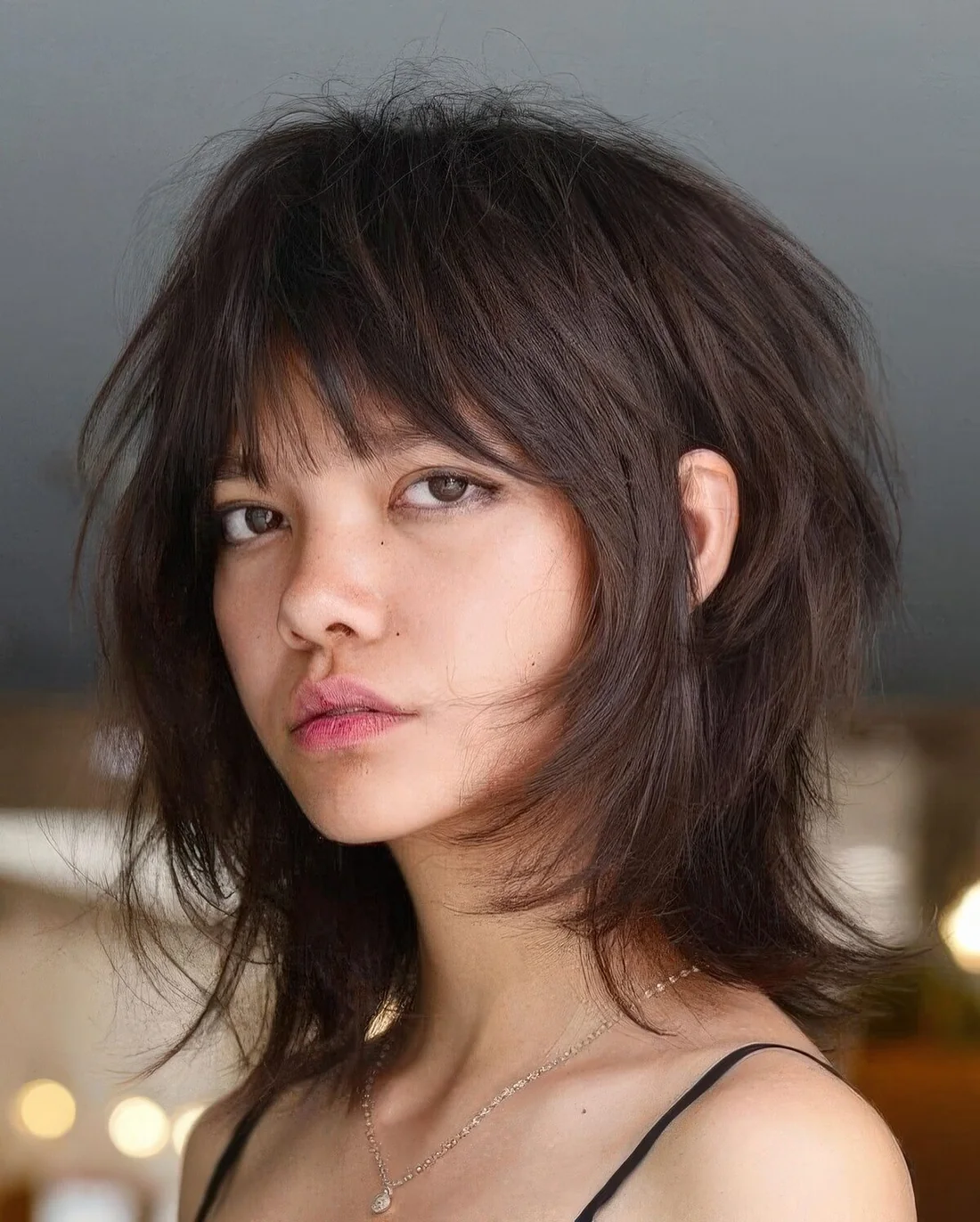 Dark brunette medium wolf cut with wispy bangs and messy volume.